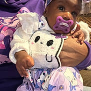 Khalani is registered to the contest to win money with this photo: baby, child, pacifier, purple_clothing, headband, hand, person, hoodie, indoor, curtains, patterned_clothing, cute, holding, portrait, infant, soft_lighting, face, expression, sitting, cozy