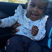 Khalani joined the competition — help win amazing prizes! child, toddler, smiling, happy, person, clothing, hair_bow, car_seat, seatbelt, jeans, baby, hand, face, portrait, indoor, window, sunlight, jacket, white_blanket, holding