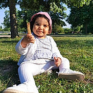Elena participe au concours pour gagner de l'argent avec cette photo : toddler, child, grass, park, trees, sunlight, outdoor, pink_bonnet, white_cardigan, striped_dress, white_leggings, white_shoes, stick, pacifier, smiling, sitting, nature, daylight, cute, face