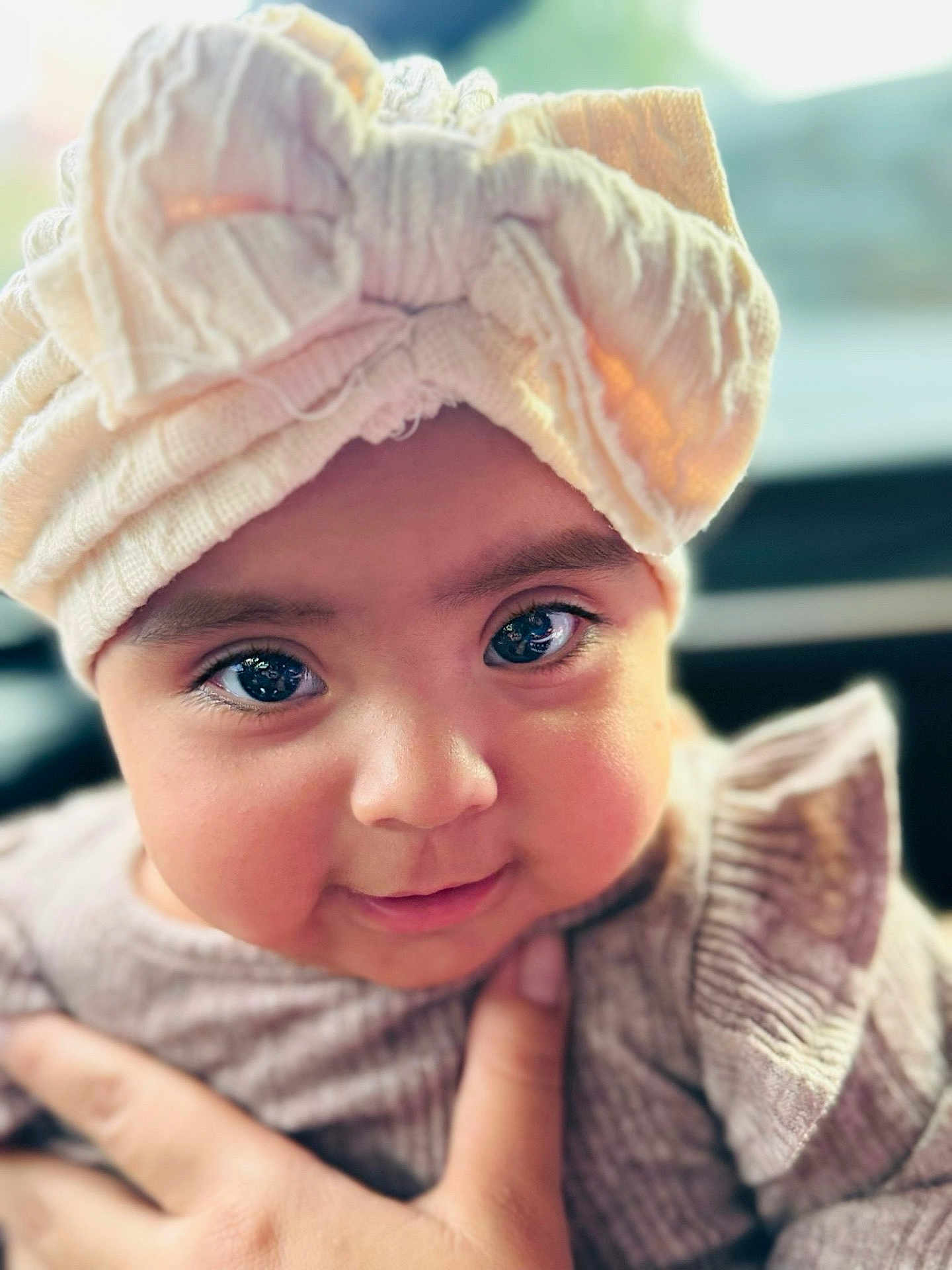 Amira joined the competition — help win amazing prizes! baby, child, face, eyes, head_wrap, knitted_clothing, hand, chubby_cheeks, closeup, portrait, cute, infant, smile, soft_lighting, indoors, warm_colors, skin, person, young_child, adorable