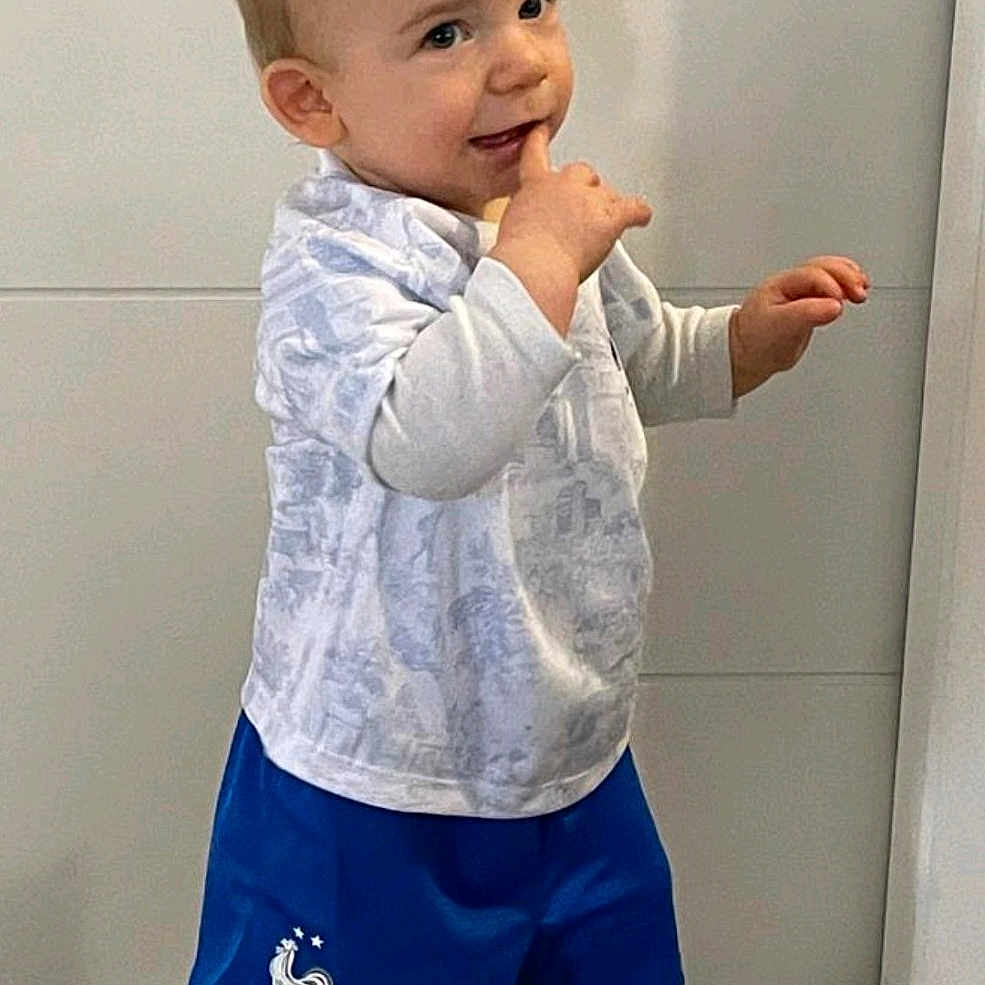Peïo a rejoint le concours — aidez-le/la à gagner de superbes lots ! blue_shorts, casual_clothing, child, cute, finger_in_mouth, floor_tiles, footwear, hair_spikes, human, indoor, light_background, person, playful, smiling, sneakers, standing, toddler, white_shirt, white_socks, young_child