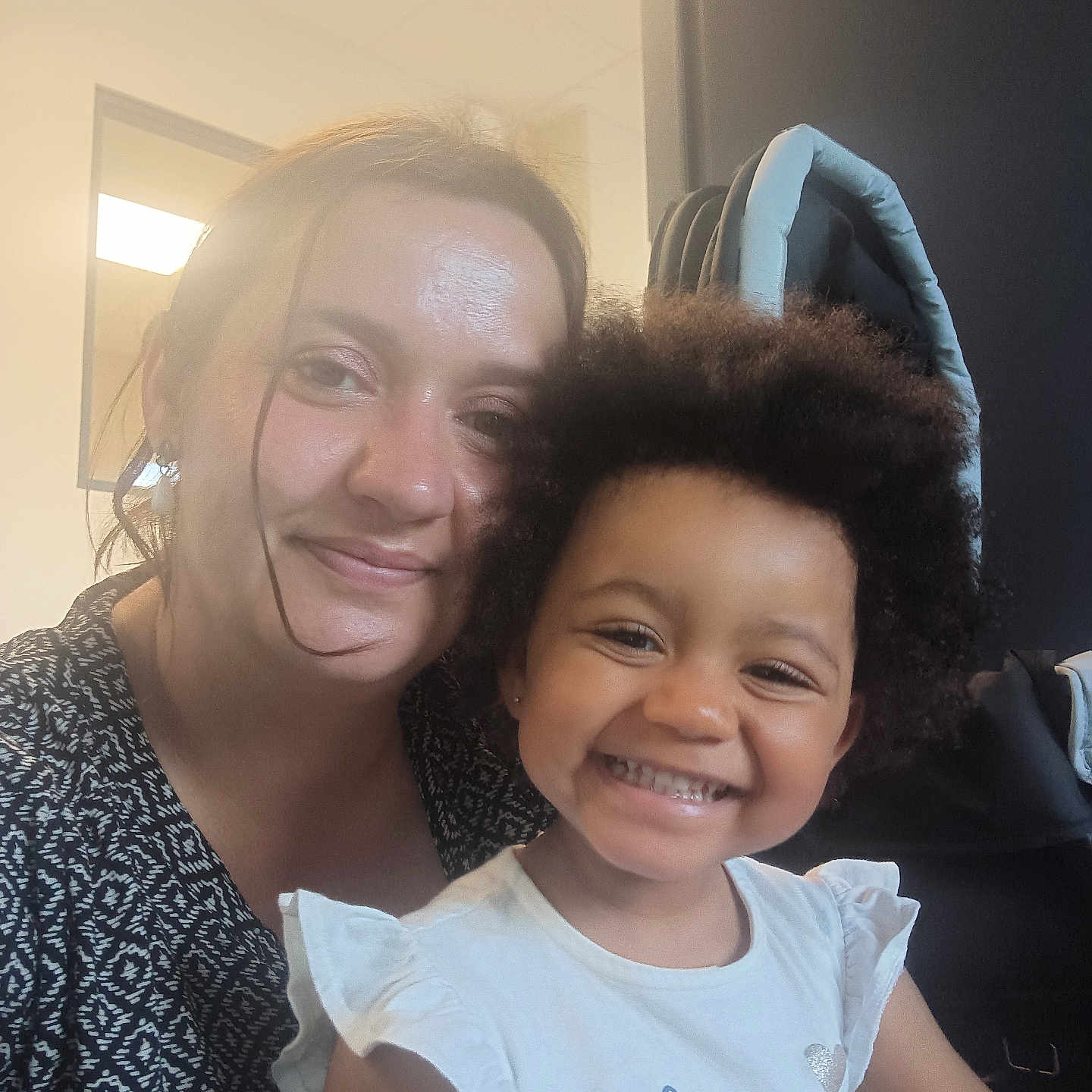 Adr participe au concours pour gagner de l'argent avec cette photo : afro_hair, black_and_white_pattern, casual_clothing, child, closeup, face, female, furniture, hair, happy, indoor, light, person, portrait, seated, smile, toddler, white_shirt, window, woman