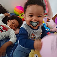Eden participe au concours pour gagner de l'argent avec cette photo : toddler, child, pacifier, plush_toy, balloon, smiling, indoor, bed, blanket, toy, person, happy, curly_hair, clothing, playtime, young_child, portrait, relaxing, colorful, casual