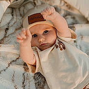 Bentley is registered to the contest to win money with this photo: baby, infant, beanie, clothing, cute, face, eyes, expression, blanket, soft_texture, pattern, lying_down, raising_arms, indoor, portrait, child, skin, warm_colors, casual_wear, adorable