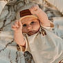 baby, infant, beanie, clothing, cute, face, eyes, expression, blanket, soft_texture, pattern, lying_down, raising_arms, indoor, portrait, child, skin, warm_colors, casual_wear, adorable