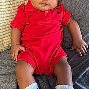 Jahlil joined the competition — help win amazing prizes! baby, infant, red_onesie, white_socks, blue_socks, nike_logo, couch, striped_pillow, indoor, child, portrait, smiling, cute, relaxed, sitting, clothing, feet, hand, face, young