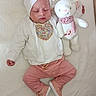 baby, sleeping, infant, white_blanket, stuffed_animal, teddy_bear, pink_pants, white_sweater, headwrap, bow, soft_toy, cute, cozy, child, indoors, resting, peaceful, comfortable, newborn, plush