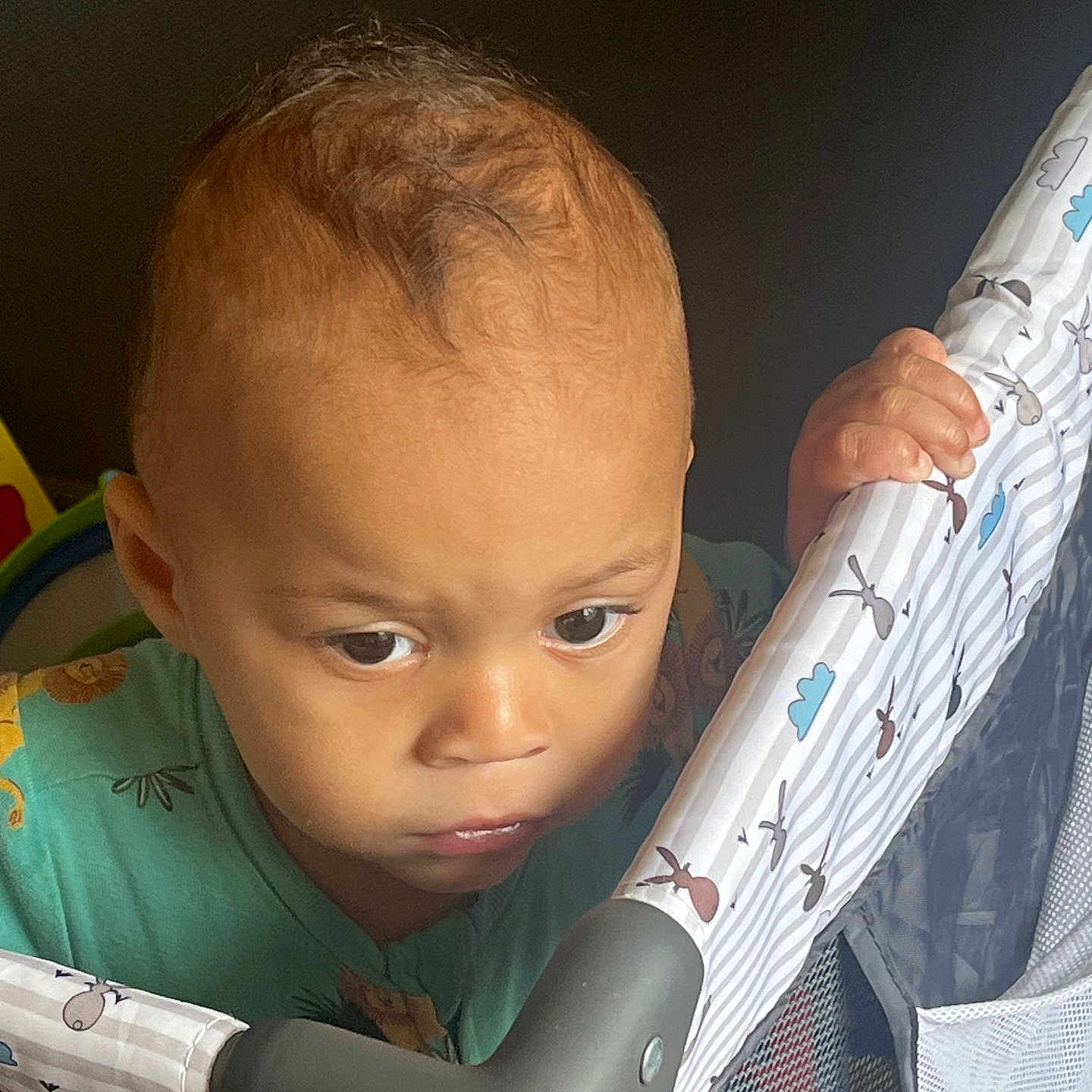 Christian joined the competition — help win amazing prizes! toddler, child, face, hand, playpen, fabric, pattern, clothing, green_shirt, curly_hair, indoor, portrait, expression, grip, baby, person, young, looking_down, closeup, soft_light