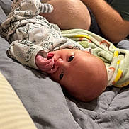 William joined the competition — help win amazing prizes! baby, infant, person, bed, blanket, onesie, hand, face, adult, phone, casual, indoor, soft, cozy, patterned_clothing, lying_down, curious, skin, family, relaxation