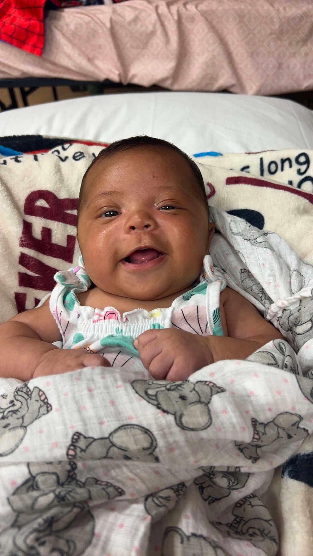 Amarah is registered to the contest to win money with this photo: baby, smiling, blanket, elephant_pattern, infant, happy, bed, pillow, clothing, cute, child, face, portrait, indoors, cozy, comfort, young, skin, hands, lying_down