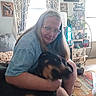 Bandit is registered to the contest to win money with this photo: woman, dog, indoor, living_room, glasses, hugging, furniture, curtains, photograph, plant, carpet, family, lamp, window, shelf, decor, portrait, casual, pet, home