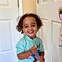 Noah is registered to the contest to win money with this photo: child, curly_hair, cute, door, floor, graphic_tshirt, happy, holding_object, indoor, joyful, person, plastic_bag, playful, shirt, shorts, smile, standing, striped_shorts, toddler, young_child