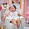 baby, child, birthday, party_hat, armchair, pink, decorations, cake, toys, smiling, happy, clothing, shoes, plush_toy, celebration, indoor, festive, cute, infant, portrait