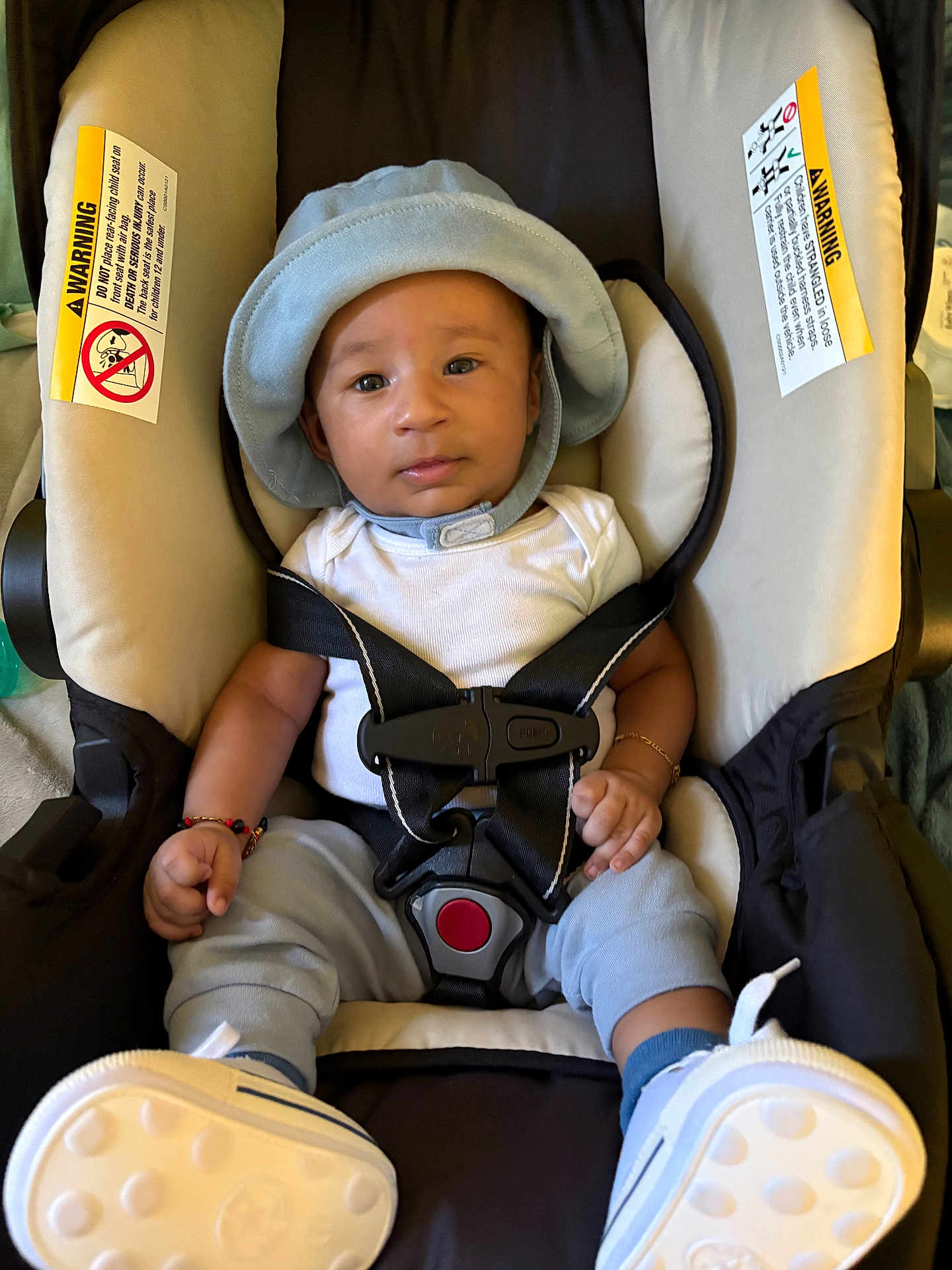 Zion joined the competition — help win amazing prizes! baby, car_seat, infant, hat, bracelet, white_shirt, blue_pants, blue_socks, footwear, straps, safety_harness, child, indoors, seat, cute, person, young_child, portrait, closeup, comfortable