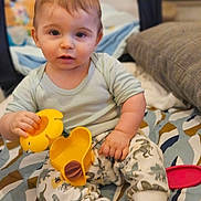 Mariùs a rejoint le concours — aidez-le/la à gagner de superbes lots ! baby, blanket, child, clothing, cozy, curious, dinosaur_pants, expression, face, hand, indoor, pattern, pillow, play, sitting, soft, toddler, toy, yellow, young