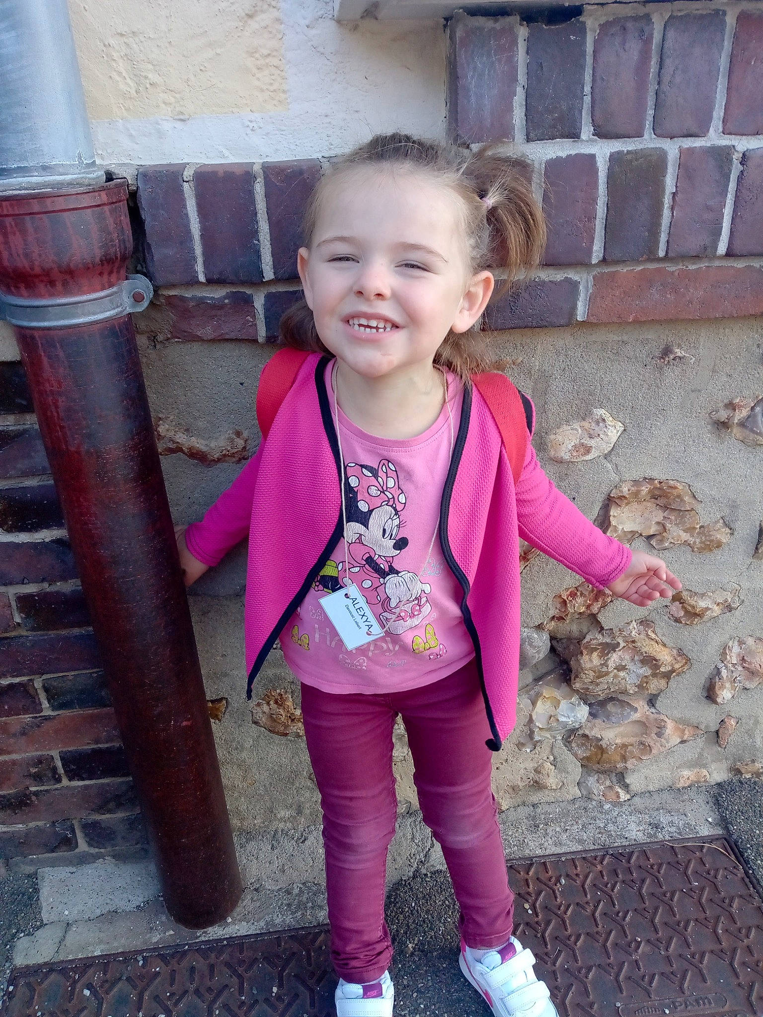 Alexya a rejoint le concours — aidez-le/la à gagner de superbes lots ! baby_toddler_clothing, brick, brickwork, child, face, fun, happy, joy, leggings, leisure, magenta, pattern, person, pink, purple, sleeve, smile, sock, standing, t_shirt