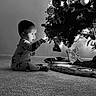 toddler, child, baby, christmas_tree, lights, ornaments, pajamas, carpet, indoor, holiday, decorations, gifts, curious, sitting, reaching, black_and_white, cozy, festive, young_child, cute