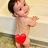 toddler, child, bathtub, bathroom, floor, tile, smile, face, hair, skin, feet, hand, water, curious, standing, red_heart, emoji, naked, cute, baby