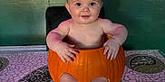 Love is registered to the contest to win money with this photo: baby, pumpkin, table, mosaic, green_wall, neon_sign, pink_light, child, smiling, bare_chest, feet, hands, indoor, decor, face, sitting, cute, holiday, autumn, playful