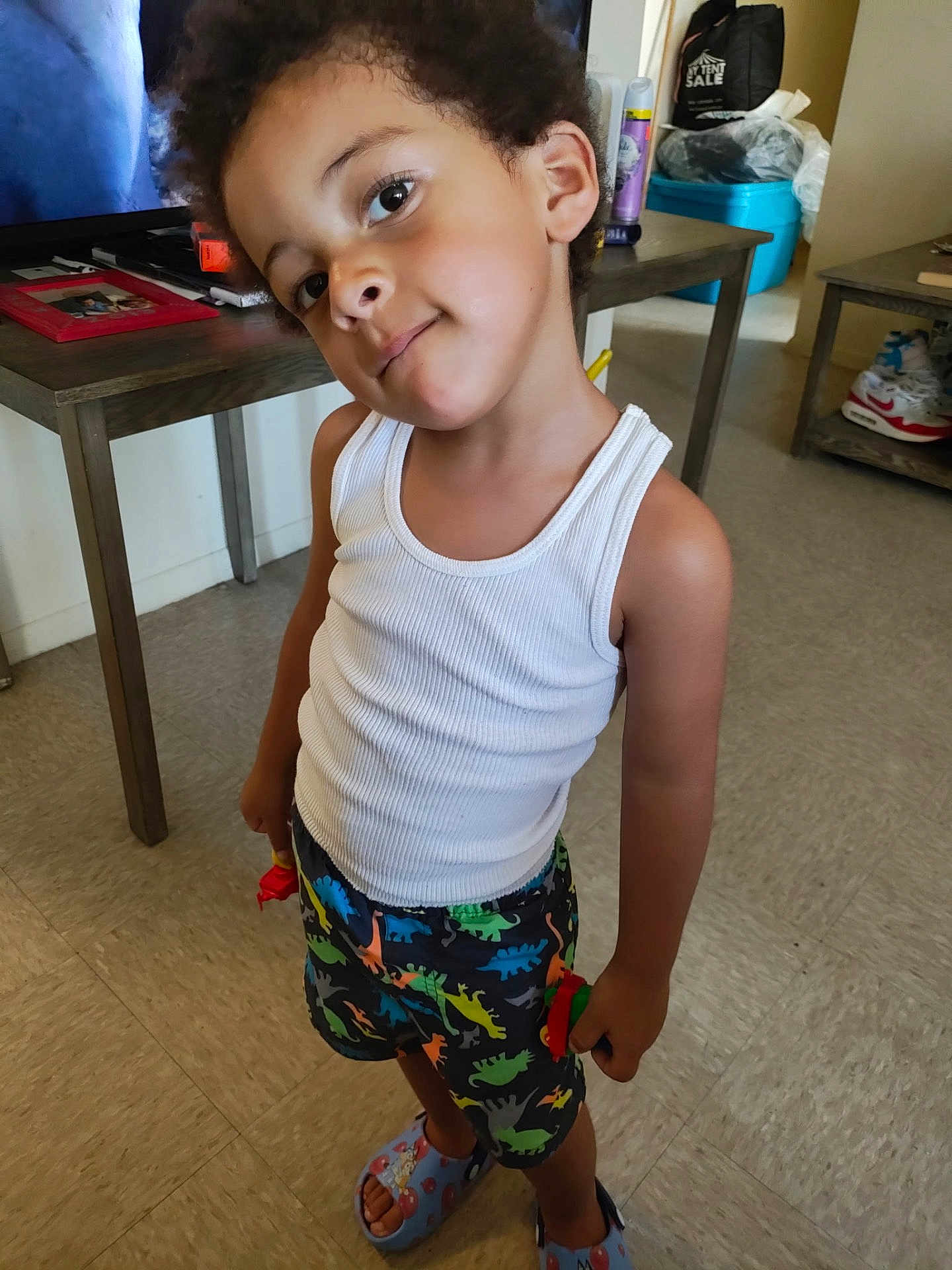 Bleu Enzo Caban joined the competition — help win amazing prizes! child, kid, indoor, floor, table, television, shorts, tank_top, slippers, dinosaur_pattern, smile, face, hair, playful, toy, furniture, room, person, standing, casual