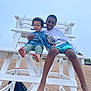 child, children, beach, sand, lifeguard_chair, white_chair, smile, barefoot, casual_clothing, outdoor, cloudy_sky, playful, friendship, summer, fun, young, portrait, two_people, sitting, relaxed