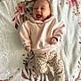 adorable, animal_print_pants, baby, blanket, child, cozy, cute, floral_pattern, happy, headband, indoors, infant, lying_down, pink_sweater, playful, portrait, smiling, socks, soft_texture, warm_colors