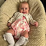 Remi is registered to the contest to win money with this photo: baby, infant, smiling, knitted_cardigan, dress, patterned_clothing, white_socks, bows, plush_cushion, beige, texture, indoor, portrait, cute, child, happy, sitting, cozy, soft, comfortable