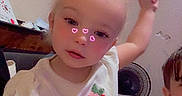 Chloe joined the competition — help win amazing prizes! toddler, child, indoor, white_shirt, strawberry_patch, pink_headband, hearts_filter, face, person, casual_clothing, shorts, fan, bed, household_items, cute, playful, blonde_hair, sitting, young_child, holding_object