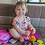 backpack, barefoot, brown_couch, child, colorful_toys, couch, cute, happy, indoor, minnie_mouse, natural_light, person, phone_toy, pink_shirt, playtime, sitting, smiling, toddler, toy, window