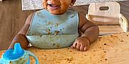 Namari joined the competition — help win amazing prizes! toddler, child, messy, food, spaghetti, sippy_cup, bib, table, wooden_table, smile, face, hands, indoor, room, chair, floor, clothing, happy, curly_hair, baby