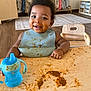 toddler, child, messy, food, spaghetti, sippy_cup, bib, table, wooden_table, smile, face, hands, indoor, room, chair, floor, clothing, happy, curly_hair, baby