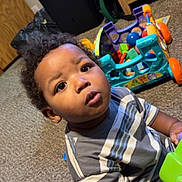 Namari is registered to the contest to win money with this photo: toddler, child, indoor, carpet, toy, colorful, furniture, wood, curly_hair, striped_shirt, playing, floor, young_child, baby, person, expression, eyes, hands, cabinets, room