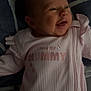 baby, infant, smile, pink_clothing, blanket, lying_down, portrait, face, child, cute, happy, newborn, soft_lighting, text_on_clothing, fabric, home, closeup, person, sleepwear, cozy