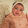 baby, infant, headband, clothing, orange_checkered, buttoned_shirt, blanket, soft_fabric, face, eyes, smile, indoor, portrait, cute, child, newborn, person, lying_down, cozy, expression