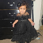 Eliana joined the competition — help win amazing prizes! child, girl, black_dress, headband, indoor, carpet, dresser, vacuum_cleaner, furniture, portrait, person, footwear, expression, standing, home, room, carpeted_floor, dress, accessory, cute