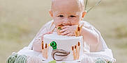 Carter is registered to the contest to win money with this photo: baby, high_chair, cake, party_hat, balloon, outdoor, grass, celebration, tassel_banner, duck, half_birthday, child, foot, hand, face, cute, food, event, festive, infant
