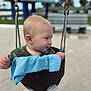 baby, swing, playground, child, outdoor, blond_hair, blue_towel, shorts, green_shirt, sand, metal_chains, seat, park, summer, daylight, curious, infant, cute, seat_swing, fun