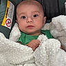 baby, infant, child, portrait, face, eyes, wide_eyed, looking_at_camera, sitting, car_seat, blanket, white_blanket, green_shirt, plush, cozy, indoor, close_up, photography, warning_label, safe
