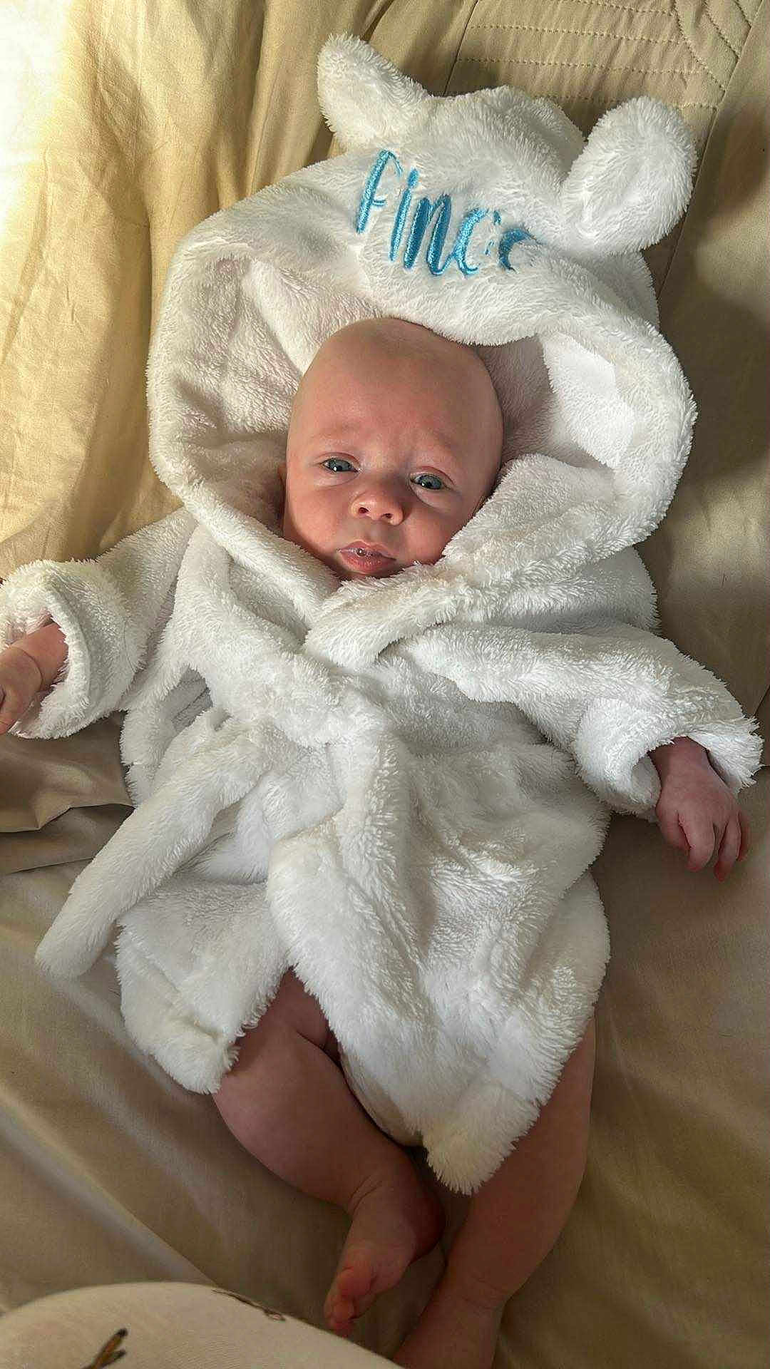 Cassius is registered to the contest to win money with this photo: baby, infant, robe, white, fluffy, hood, ears, bed, blanket, skin, face, legs, arms, cute, cozy, lying, soft, child, indoors, sleepwear