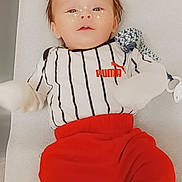 Kayson is registered to the contest to win money with this photo: baby, child, infant, puma, clothing, red_pants, striped_shirt, lying_down, face, freckles, sparkles, digital_effect, cute, portrait, indoor, soft_lighting, toy, pacifier, hands_covered, white_background