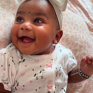 Sumara is registered to the contest to win money with this photo: baby, smiling, headband, bow, infant, cute, white_outfit, patterned_clothing, horse_print, stars, lying_down, bedspread, happy, jewelry, bracelet, earrings, closeup, portrait, child, indoor
