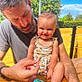 baby, man, smile, outdoor, wooden_table, toy, sunlight, playful, child, happy, beard, casual_clothing, summer, nature, greenery, person, family, daylight, fun, portrait
