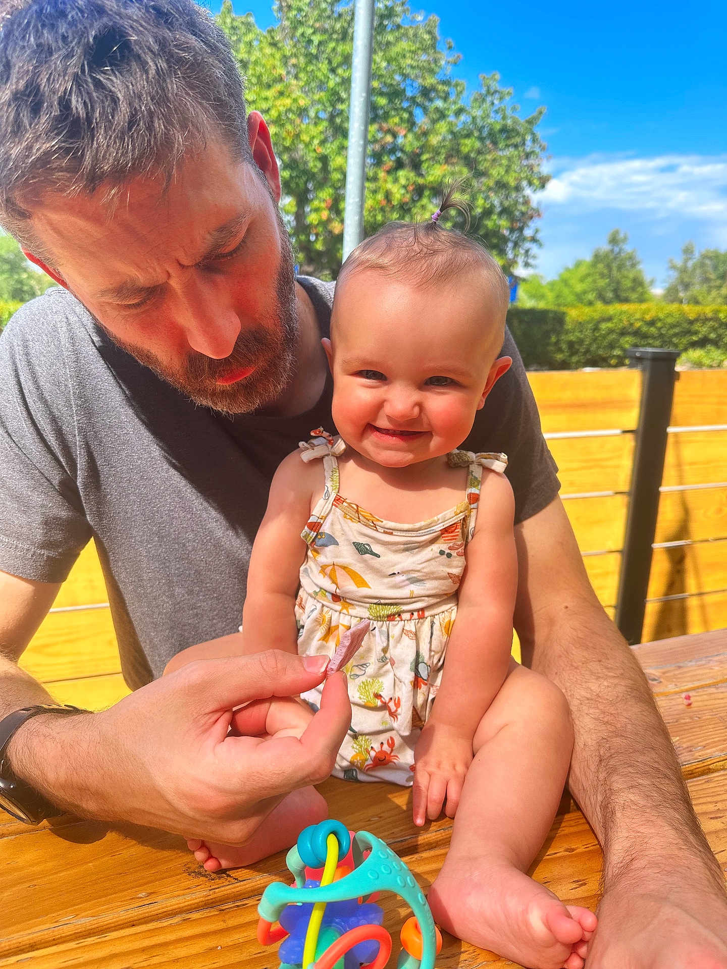 Addie joined the competition — help win amazing prizes! baby, man, smile, outdoor, wooden_table, toy, sunlight, playful, child, happy, beard, casual_clothing, summer, nature, greenery, person, family, daylight, fun, portrait