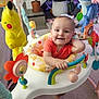 baby, activity_center, toy, colorful, smiling, indoor, child, plant, home, floor, foot, face, clothing, orange_shirt, plastic, seat, play, happy, cute, infant