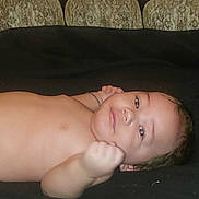 Angel is registered to the contest to win money with this photo: baby, infant, face, skin, hand, fist, lying_down, couch, pattern, expression, curious, indoor, child, portrait, young, human, head, eyes, mouth, cheeks
