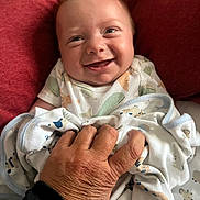 Anthony joined the competition — help win amazing prizes! baby, smiling, face, hand, blanket, cushion, red, clothing, person, infant, cozy, comfort, portrait, cute, happy, wrapped, animal_print, skin, warmth, closeup