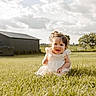 baby, child, infant, smiling, happy, portrait, outdoor, grass, field, countryside, barn, farm, dress, white_clothing, curly_hair, sitting, sunlight, cloudy_sky, nature, rural_landscape
