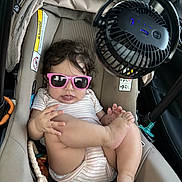 Alice is registered to the contest to win money with this photo: baby, infant, child, sunglasses, pink_sunglasses, car_seat, car, vehicle, fan, clip_on_fan, seated, indoor, portrait, fashion, summer, striped_clothing, barefoot, toys, travel, safety_seat
