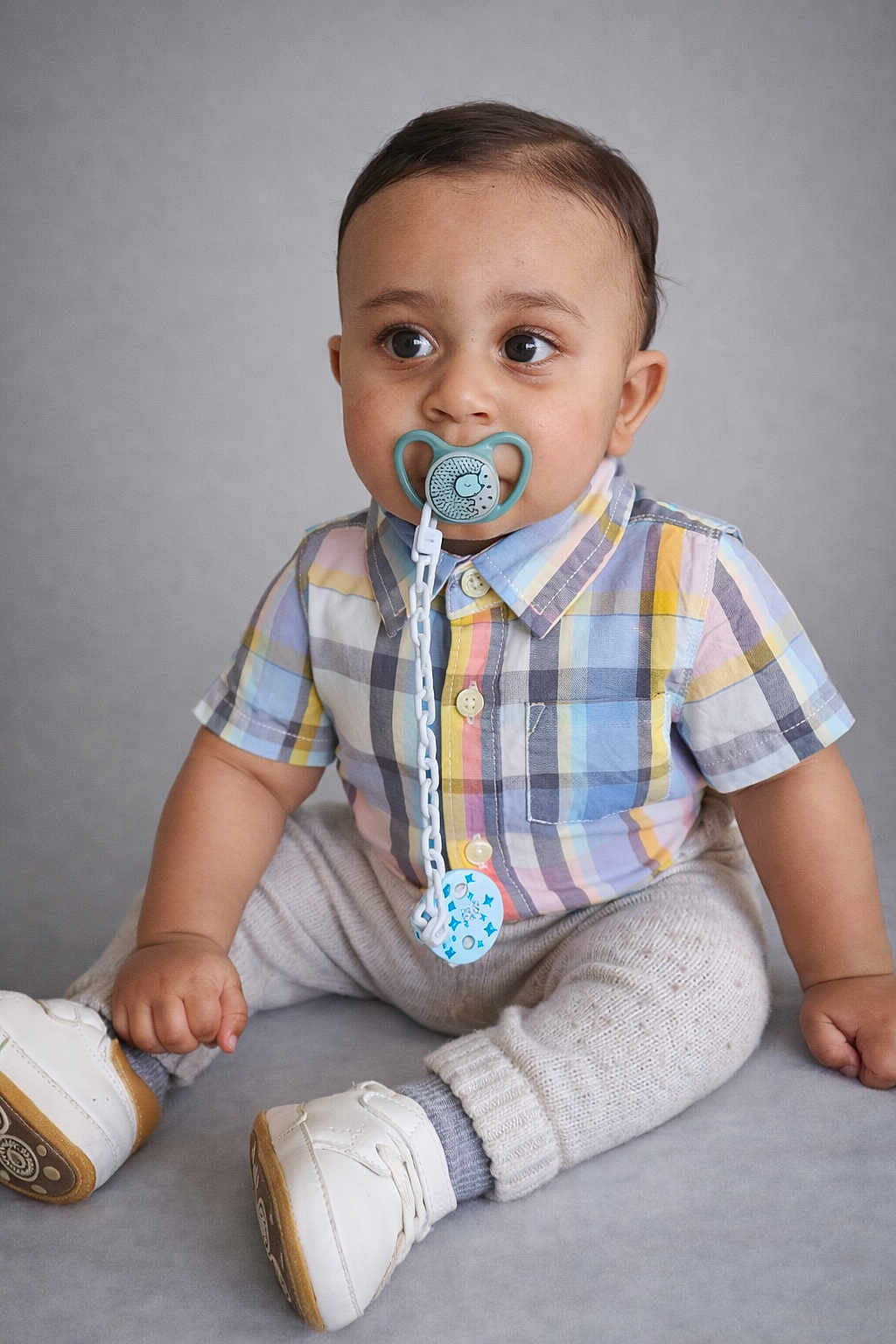 Issa participe au concours pour gagner de l'argent avec cette photo : baby, toddler, child, pacifier, pacifier_chain, plaid_shirt, button_up, sitting, sneakers, knit_pants, socks, portrait, indoor, studio_background, curious_look, big_eyes, hand, face, clothing, cute