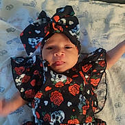 Abigail joined the competition — help win amazing prizes! baby, infant, child, black_clothing, red_roses, skulls, headband, bow, blanket, footprints, lying_down, tongue_out, cute, patterned_fabric, soft_texture, indoors, portrait, playful, young_child, face